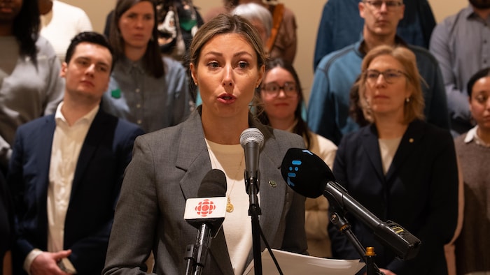 A woman speaks in front of microphones.