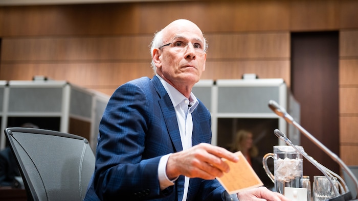 Michael Wernick tient une feuille de papier sur un bureau dans une salle d'audience.