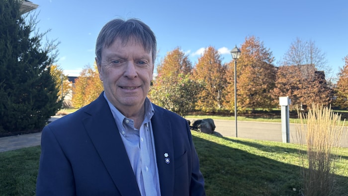 Un homme en veston devant des arbres