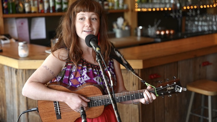 Une femme joue de la guitare et chante dans un micro.