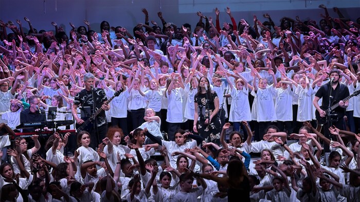 Des musiciens et un chœur de 500 enfants sur une scène.