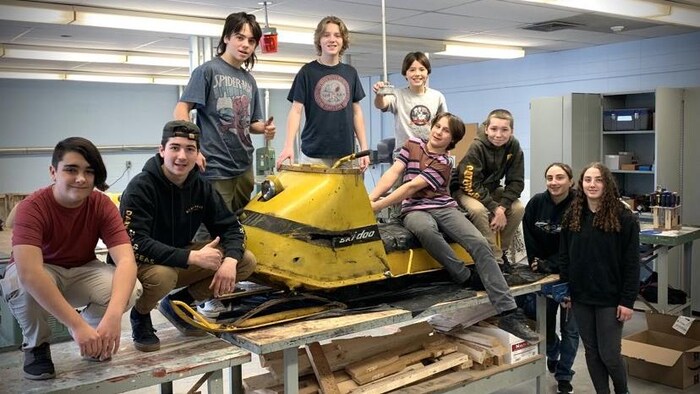 Des élèves autour d'une vieille motoneige jaune.