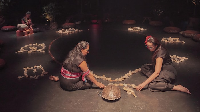 Une scène de la pièce de théâtre «Nigamon\Tunai» où deux femmes sont assises sur la scène.