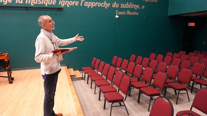 Un homme debout sur une scène devant une grande pièce remplie de chaises.