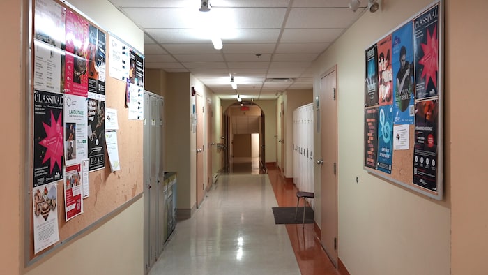 Un grand corridor avec des portes, des casiers et des babillards qui longent les murs.