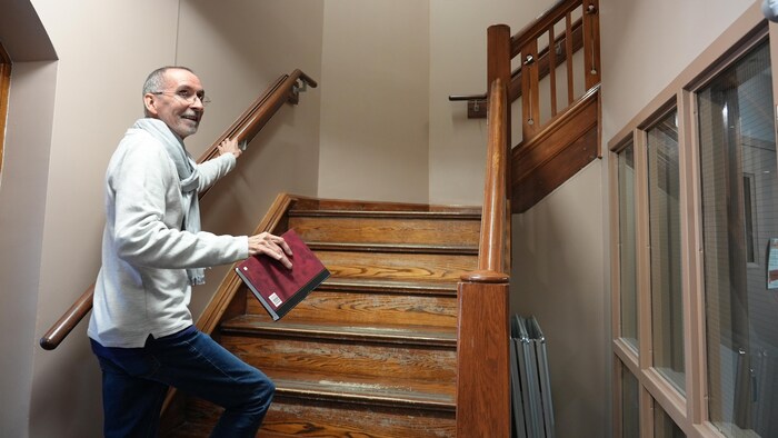 Un homme avec un grand sourire qui s'apprête à monter un escalier en bois.