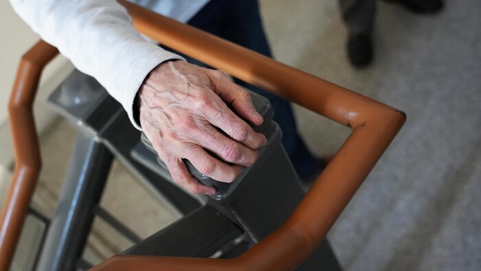 Gros plan de la main d'un homme qui est appuyée sur un poteau d'une rampe d'escalier.