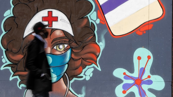 Un homme marche devant une murale représentant une travailleuse de la santé.