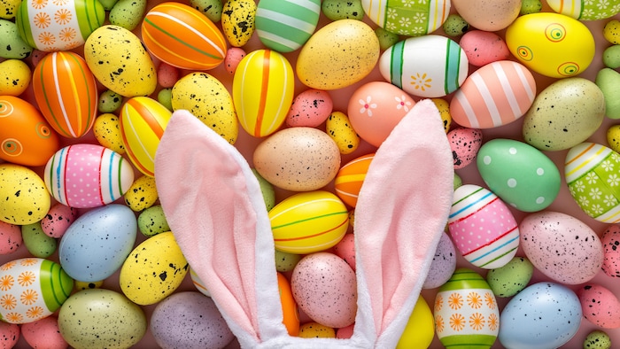 Des oreilles de lapin en peluche déposées sur des œufs de Pâques.