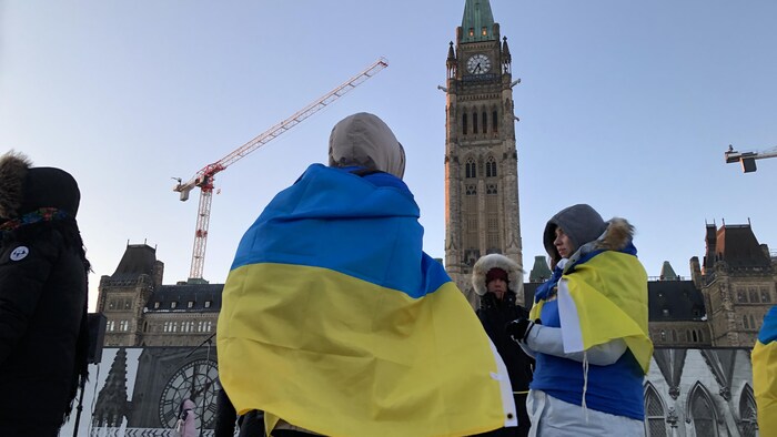 Des manifestants enroulés dans un drapeau ukrainien devant le parlement canadien.