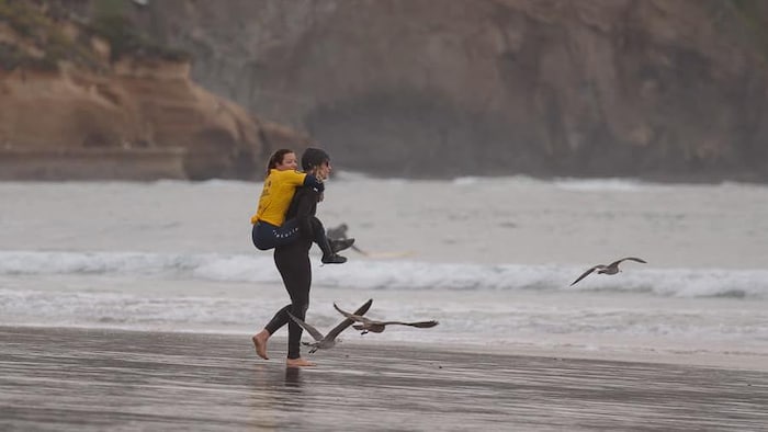 Une femme porte une surfeuse sur ses épaules. 