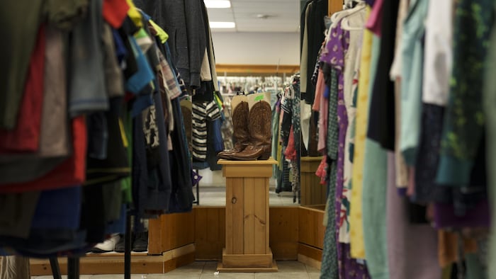 Des rayons de vêtements dans une friperie et une paire de bottes sur un podium en bois.