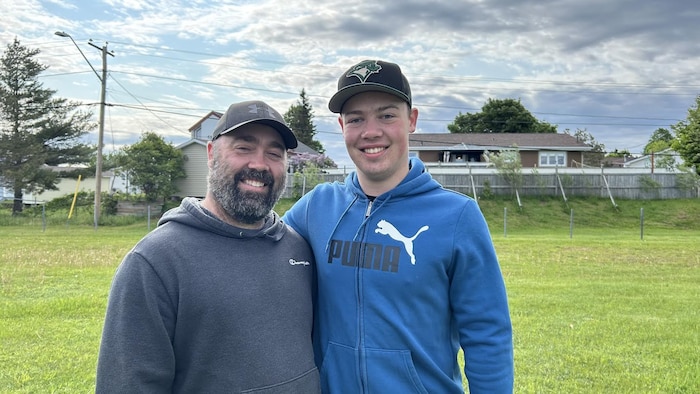 Homme avec chandail gris au côté de son fils qui a une casquette et un chandail bleu