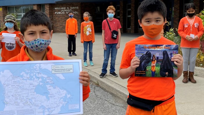 Des enfants vêtus de couleur orange tiennent une carte du Canada et des pancartes en souvenir des enfants autochtones disparus.