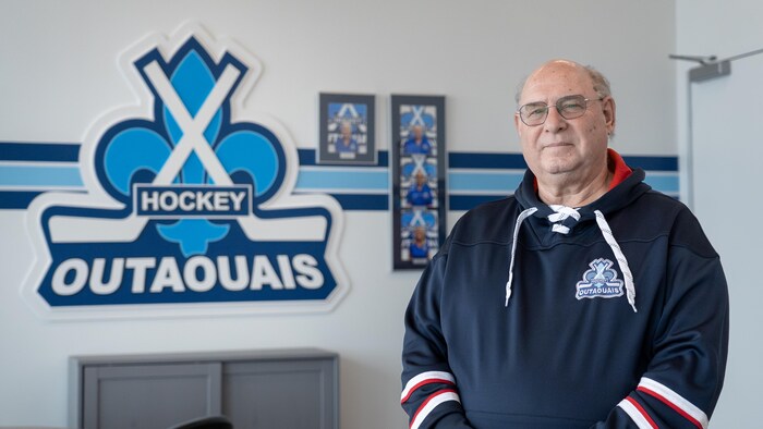 Un homme pose devant le logo de Hockey Outaouais.
