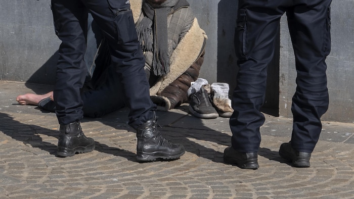 Deux policiers debout devant un homme sans-abri assis sur le bord d'un édifice.