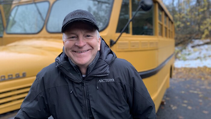 Un homme souriant devant un autobus à l'extérieur.