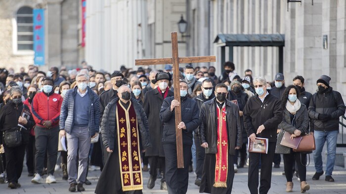 Des personnes marchent derrière une grande croix.