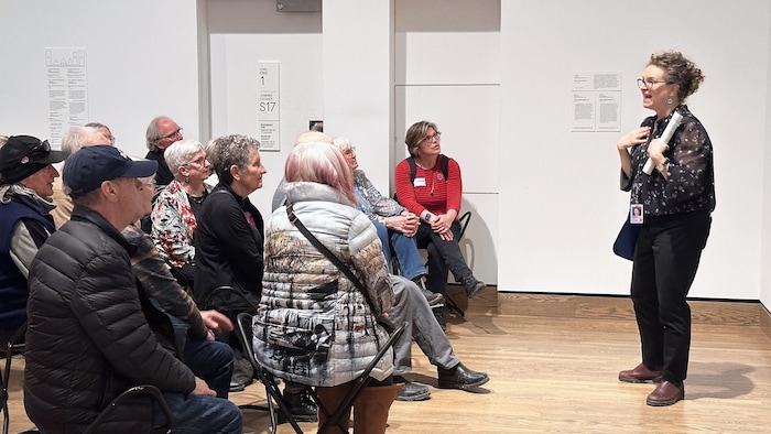 Une femme debout qui parle devant plusieurs personnes assises devant elle dans une salle du Musée des beaux-arts du Canada.