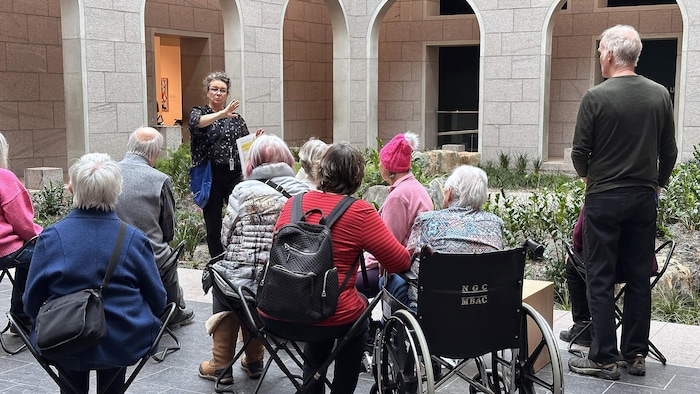 Une femme debout qui parle devant plusieurs personnes assises devant elle dans une salle du Musée des beaux-arts du Canada.