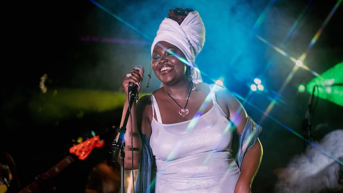 Une femme souriante en performance musicale sur une scène.