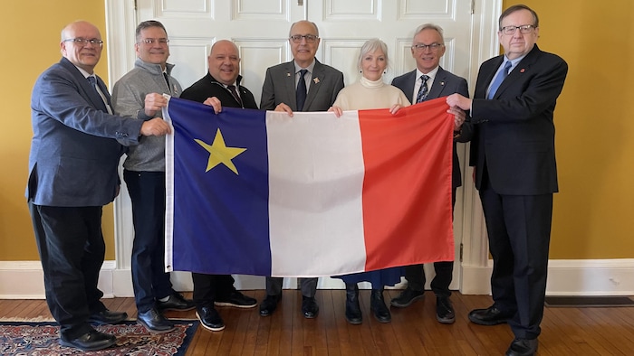 Sept personnes tenant un drapeau acadien.
