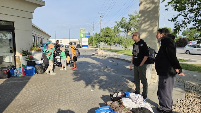 Des personnes attendent devant un hôtel avec des sacs.