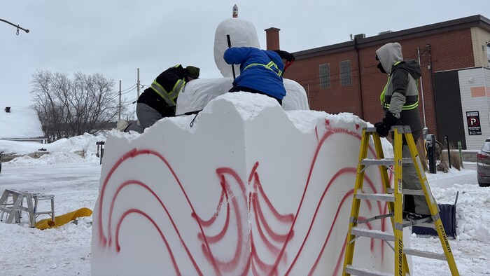 Des gens font de la sculpture sur neige, l'un est sur une échelle.