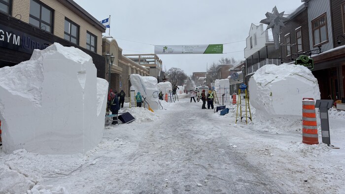 Une rue piétonne avec de grands cubes de neige et des gens qui les sculptent.