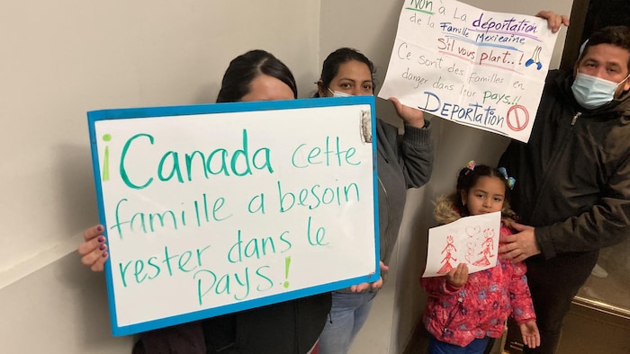 Une famille tient des affiches qui indiquent "Canada, cette famille a besoin de rester dans le pays! et Non à la déportation de la famille Mexicaine s'il vous plaît"