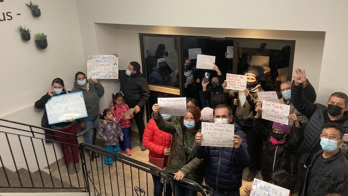 Une vingtaine de personnes tiennent des affiches pour soutenir la famille Rodriguez-Flores (ex : "Arrêtez la déportation")
