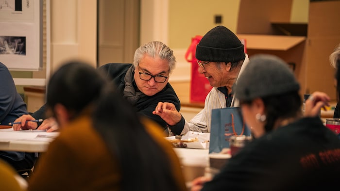 Deux hommes assis autour d'une grande table qui discute entre eux.