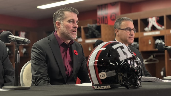 Deux hommes sont assis à une table devant des journalistes.