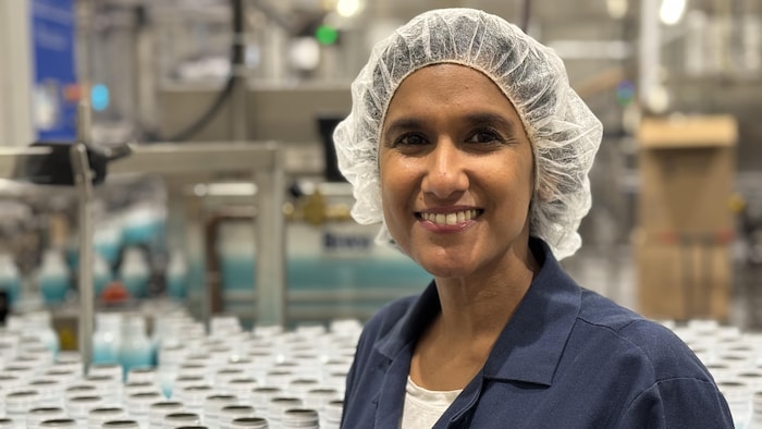 Saawan Logan sourit. Elle pose avec une blouse et un filet sur les cheveux devant une pile de bouteilles de son entreprise.