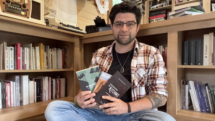 Sébastien Bérubé, assit dans sa bibliothèque, tient quelques exemplaires.