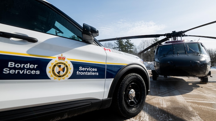 Une voiture de l'Agence des services frontaliers stationnée tout près d'un hélicoptère de la GRC.