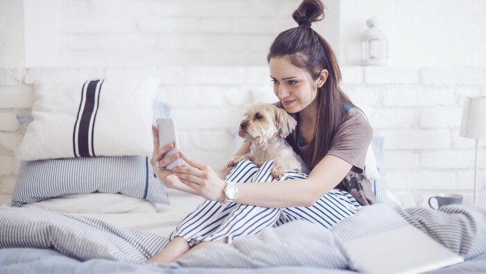 Une femme tient son chien sur elle alors qu'elle prend un égoportrait avec son téléphone intelligent. 