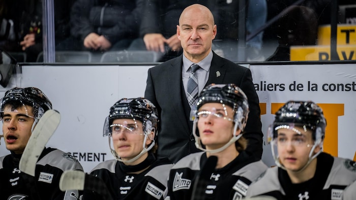 Un homme se trouve derrière le banc de son équipe durant un match de hockey.