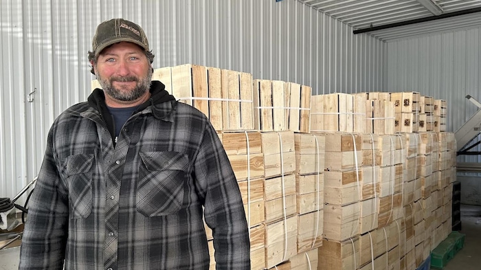 Homme avec chemise carottée devant une pile de petites caisses en bois