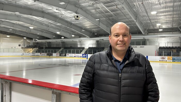 Homme devant patinoire, grand sourire, manteau noir, chemise bleue