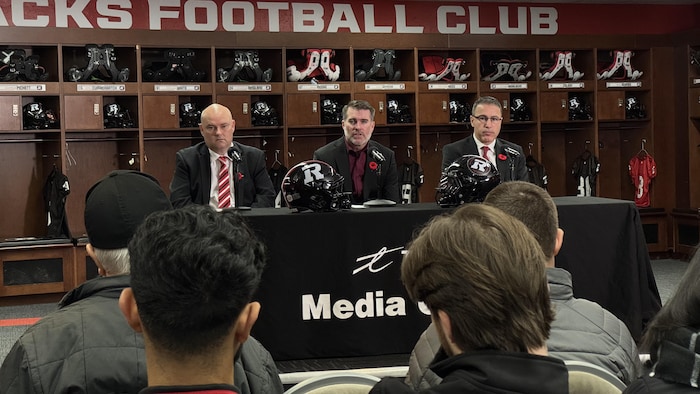 Trois hommes sont assis à une table devant des journalistes.