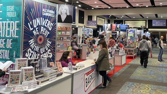 Plan ample sur les stands du Salon du livre de l'Outaouais. Des auteurs sont attablés. Des passants circulent.