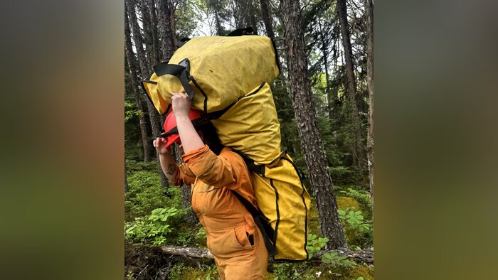 Une pompière balance trois gros sacs sur son dos et marche dans une forêt.