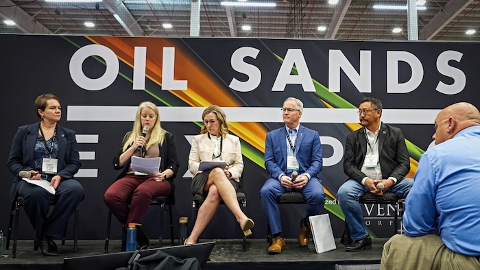 Toutes les personnes sont assises sur une scène devant un panneau disant Oil Sands.