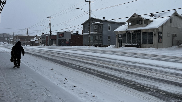 Une personne marche sur un trottoir enneigé.