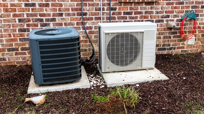Une thermopompe et un climatiseur aux côtés d'une maison en briques.