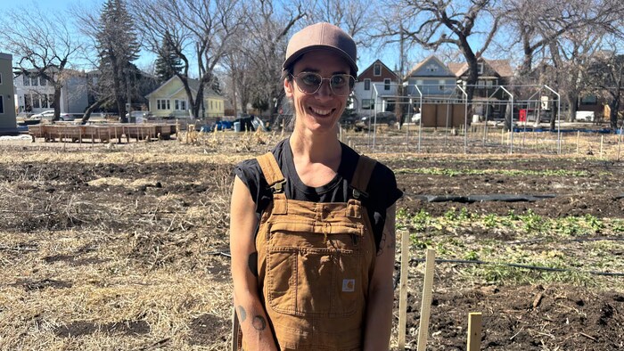 Une fermière se tient dans un champ, avec quelques maisons en arrière-plan.