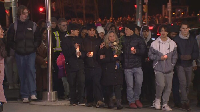 Une foule de personnes dont certaines portent des chandelles.