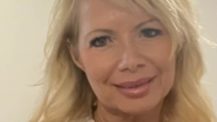 Une femme aux cheveux blonds sourit légèrement.