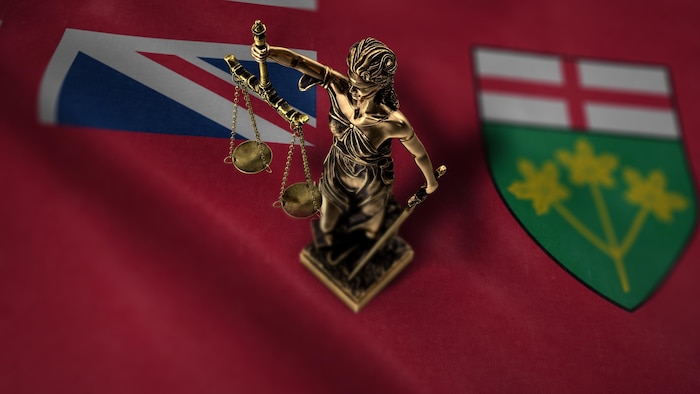 Une statue de la justice posée sur le drapeau ontarien.